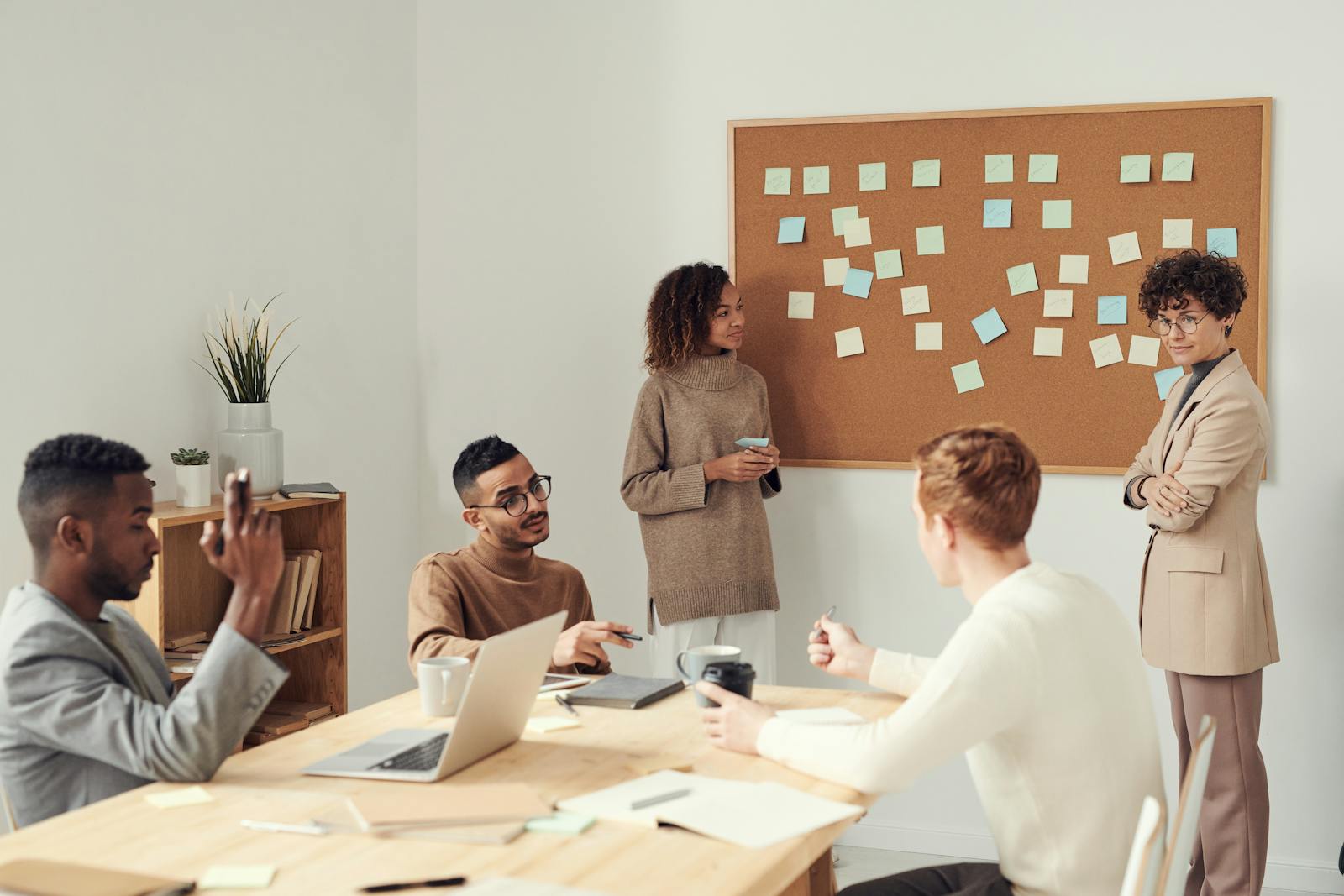 People collaborating over laptops at a table—approval, review, and lifecycle work as part of the loop, not an afterthought.